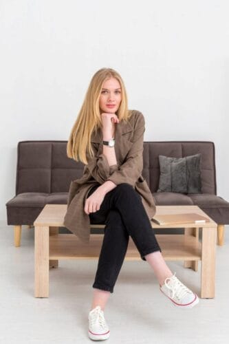 Mujer joven sentada en una mesita delante del sofá clásico de su salón de casa