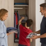 Padres ayudando a su hijo a colocar la ropa en su nuevo armario juvenil